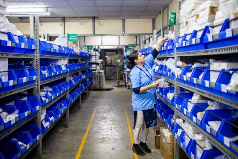 Woman in uniform organizing inventory in a warehouse aisle with labeled bins.